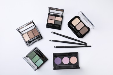Photo of Many different eye shadow palettes and professional makeup brushes on white background, flat lay