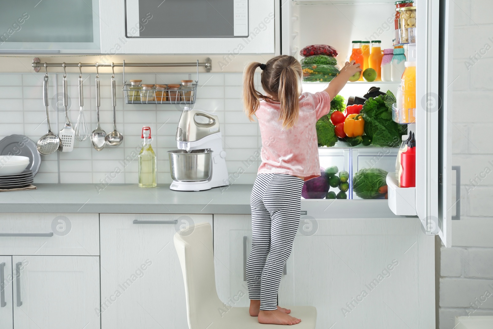 Photo of Cute girl taking apple out of refrigerator in kitchen