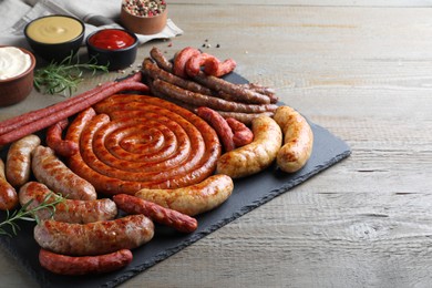 Photo of Different delicious sausages with rosemary and sauces on wooden table. Assortment of beer snacks