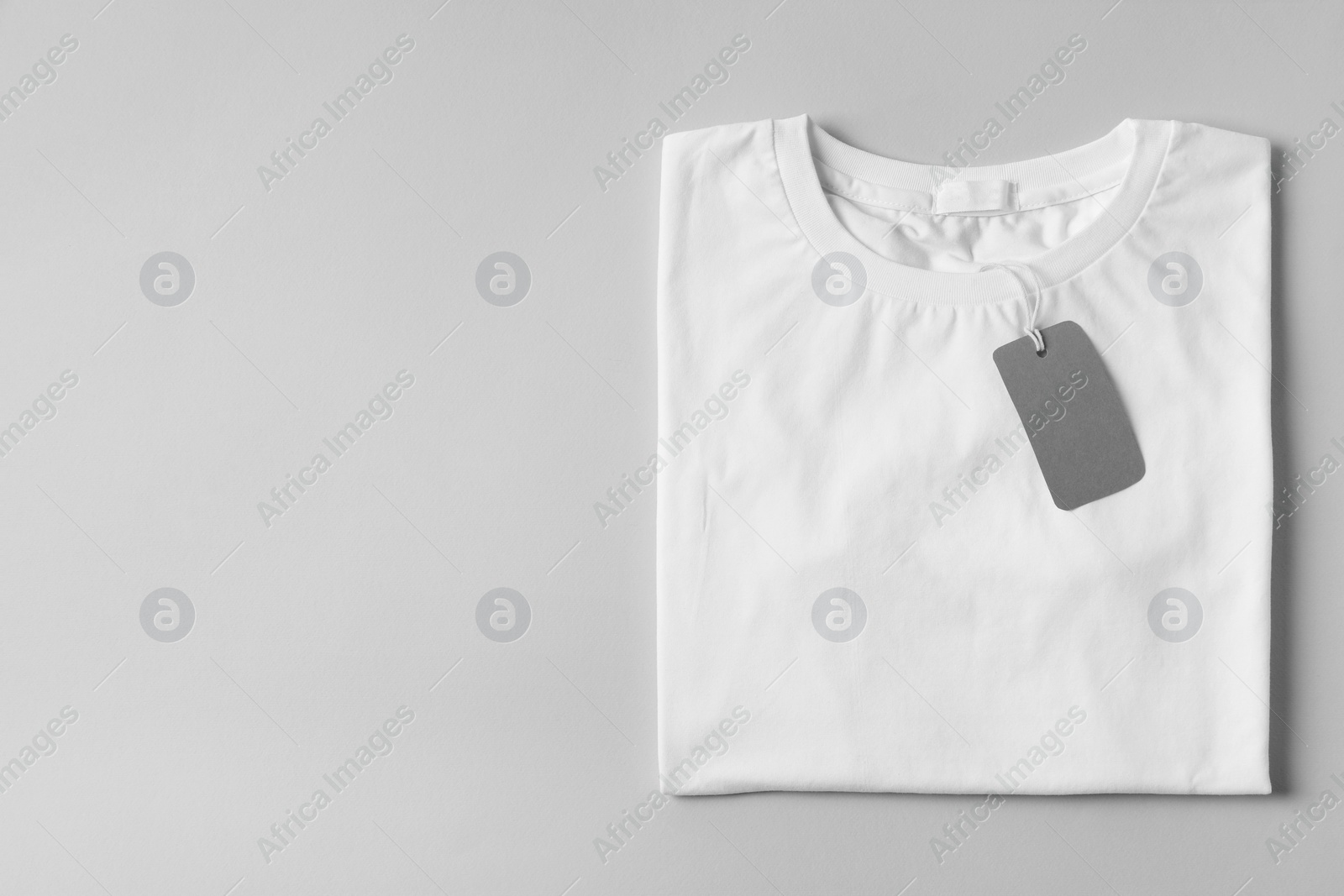 Photo of Stylish T-shirt with label on light grey background, top view. Space for text