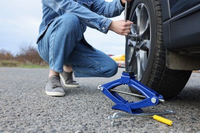 Young man changing tire of car on roadside, closeup