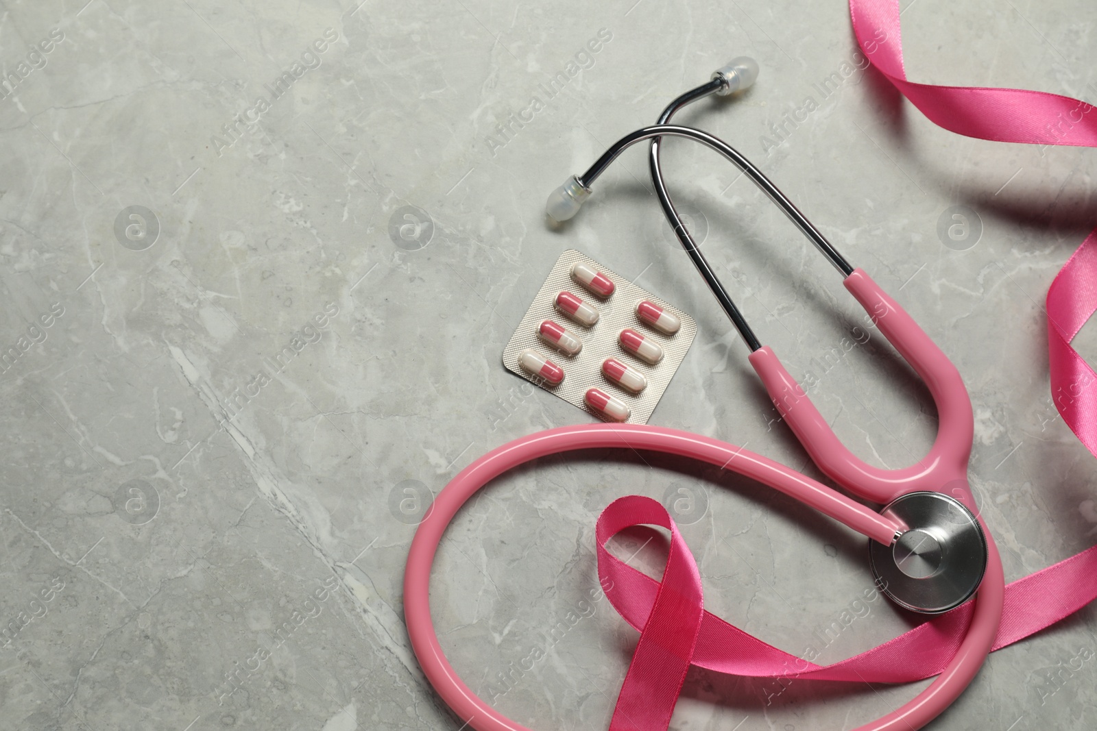 Photo of Breast cancer awareness. Pink ribbon, stethoscope and pills on grey marble table, flat lay. Space for text