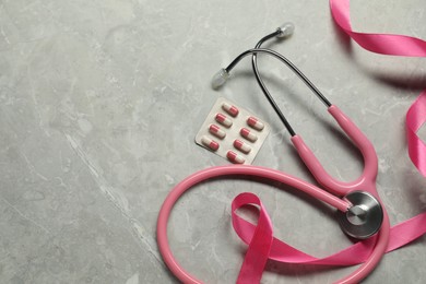 Breast cancer awareness. Pink ribbon, stethoscope and pills on grey marble table, flat lay. Space for text