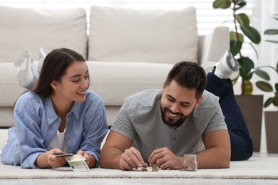 Happy young couple counting money on floor at home