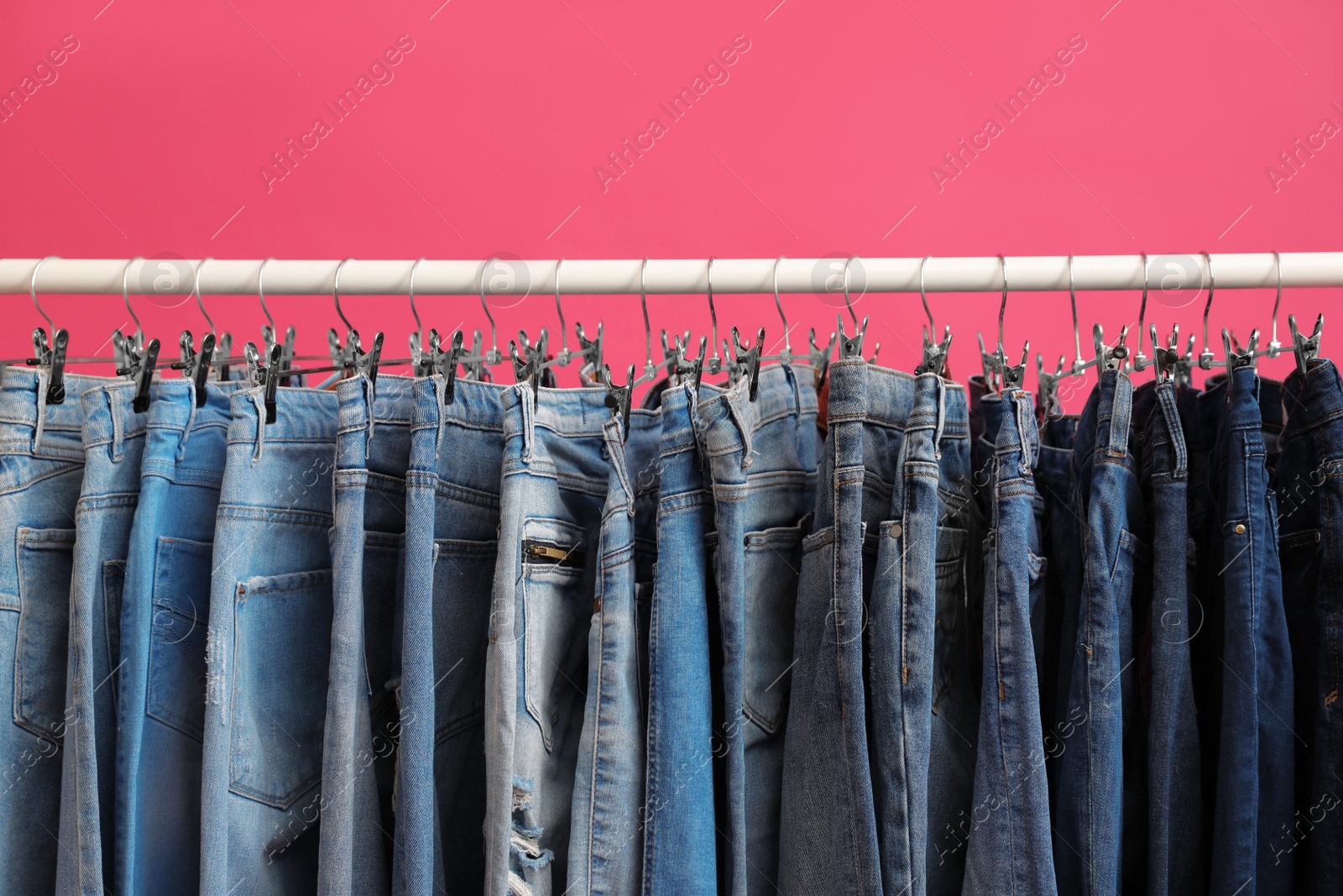 Photo of Rack with stylish jeans on pink background, closeup