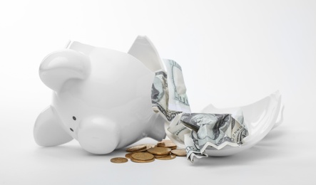 Broken piggy bank with coins and banknotes on white background