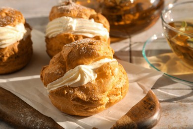 Delicious profiteroles filled with cream and tea on white tiled table, closeup