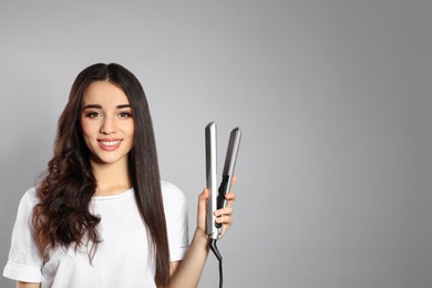 Happy woman with hair iron on grey background. Space for text