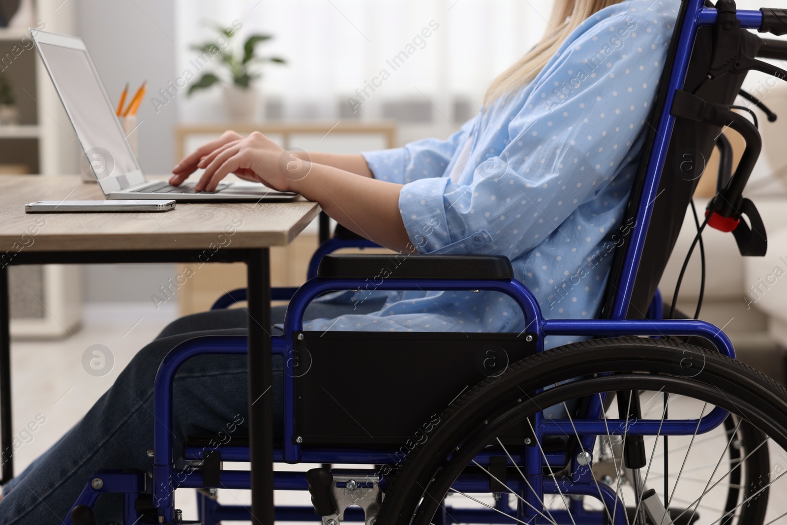 Photo of Woman in wheelchair using laptop at home, closeup