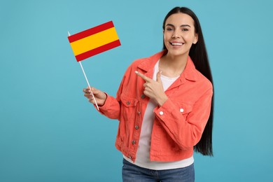 Image of Happy young woman pointing at flag of Spain on light blue background