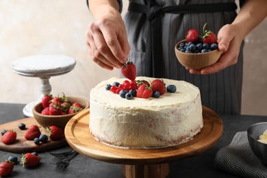 Photo of Woman decorating delicious homemade cake with fresh berries at table indoors, closeup