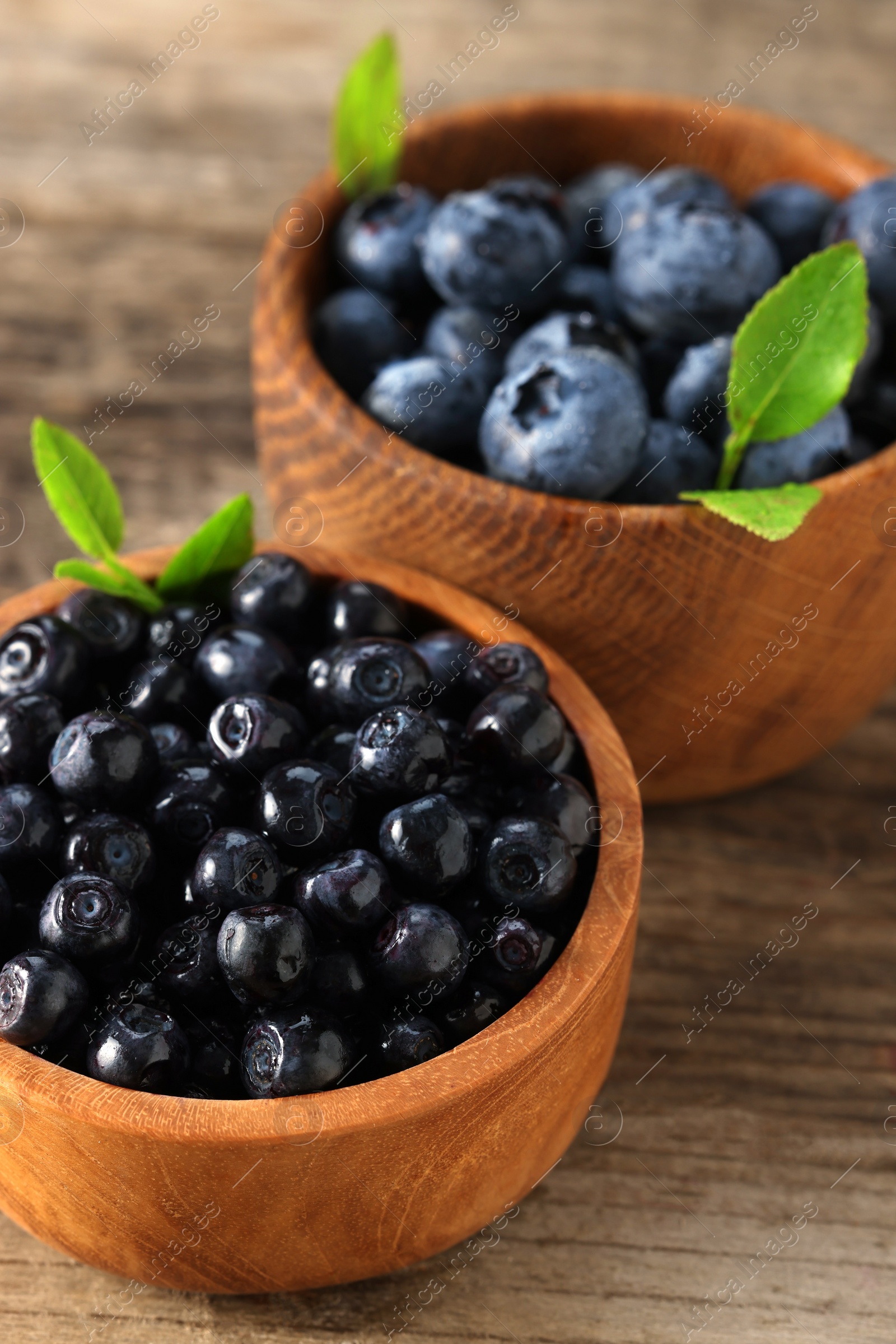 Photo of Ripe bilberries and leaves in bowls on wooden table, closeup