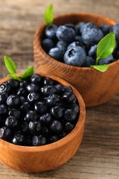 Ripe bilberries and leaves in bowls on wooden table, closeup