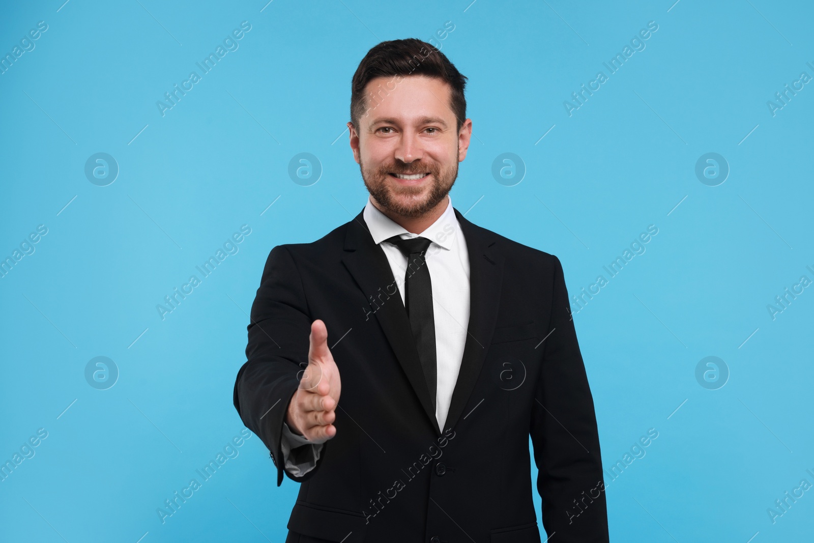 Photo of Happy man welcoming and offering handshake on light blue background