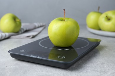 Photo of Digital kitchen scale with ripe green apple on grey table