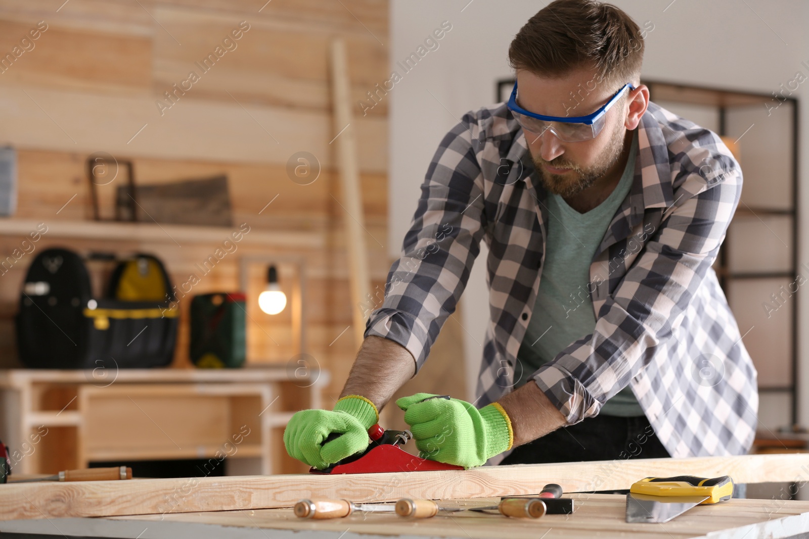 Photo of Carpenter shaping wooden bar with hand plane at table in workshop