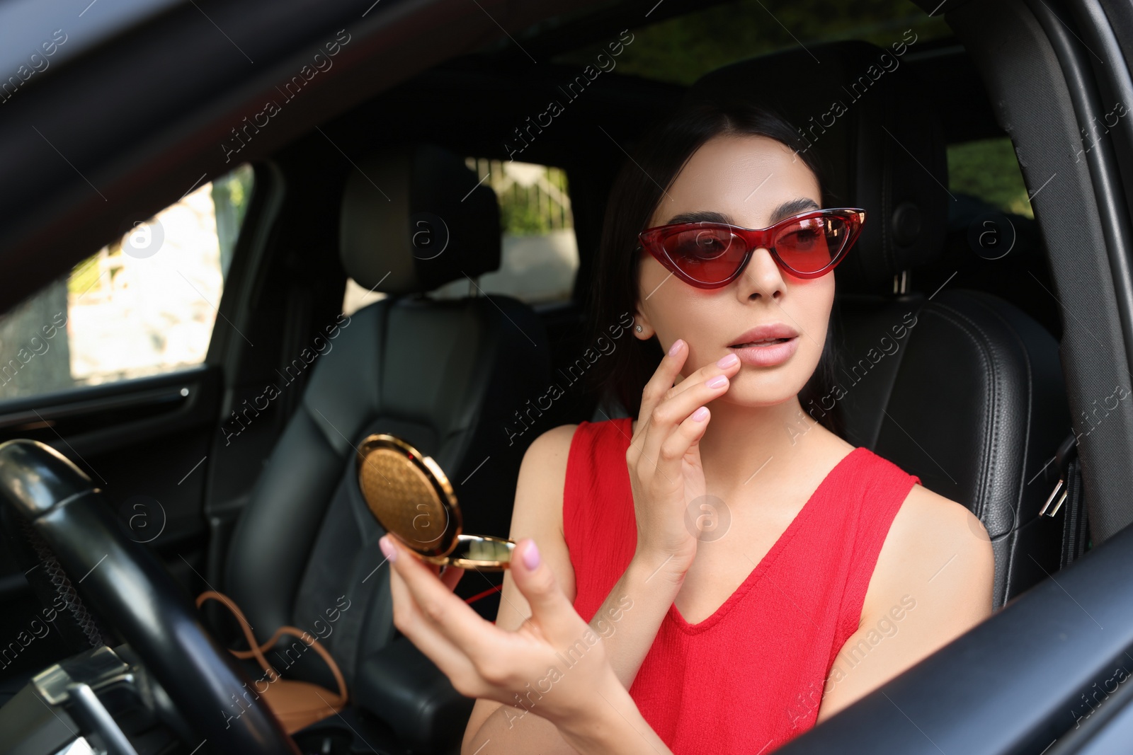 Photo of Beautiful young woman with cosmetic pocket mirror in car