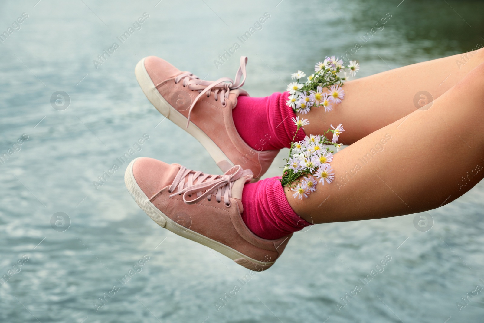 Photo of Woman with beautiful tender flowers in socks near river, closeup