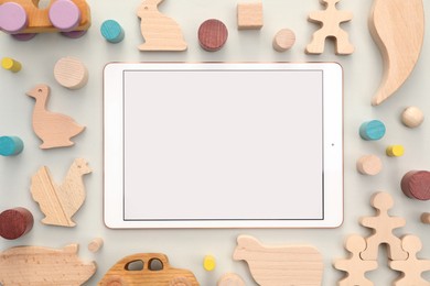 Photo of Modern tablet and wooden toys on light background, flat lay. Space for text