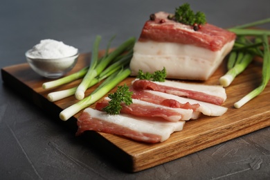 Photo of Board with pork fatback, onions and salt on black stone background, closeup