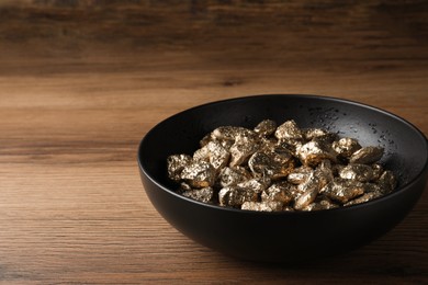 Photo of Bowl of gold nuggets on wooden table, closeup. Space for text