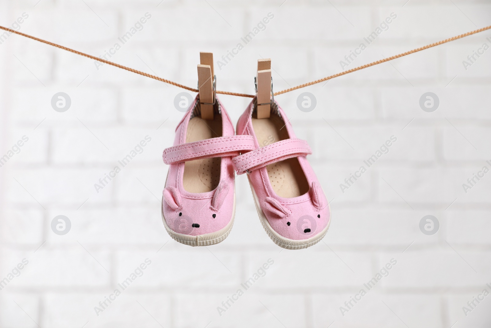Photo of Cute pink baby shoes drying on washing line against white brick wall