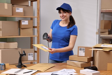 Photo of Parcel packing. Post office worker with scanner reading barcode at wooden table indoors