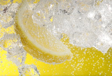 Photo of Juicy lemon slice and ice cubes in soda water against yellow background, closeup