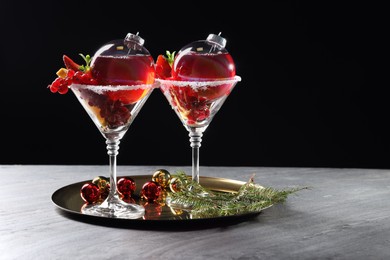 Photo of Creative presentation of Christmas Sangria cocktail in baubles and glasses on grey table against black background. Space for text