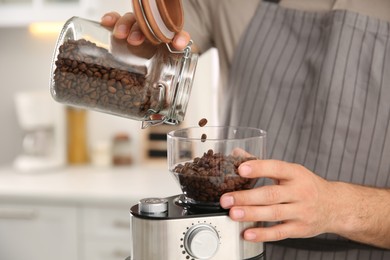 Photo of Man using electric coffee grinder in kitchen, closeup