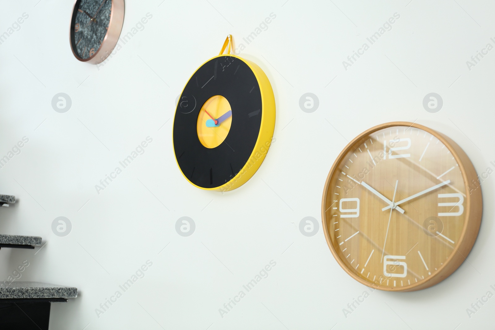 Photo of Different stylish clocks hanging on white wall. Time of day