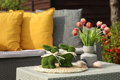 Terrace with Easter decorations. Bouquet of tulips in vase, bunny figures and decorated eggs on table outdoors