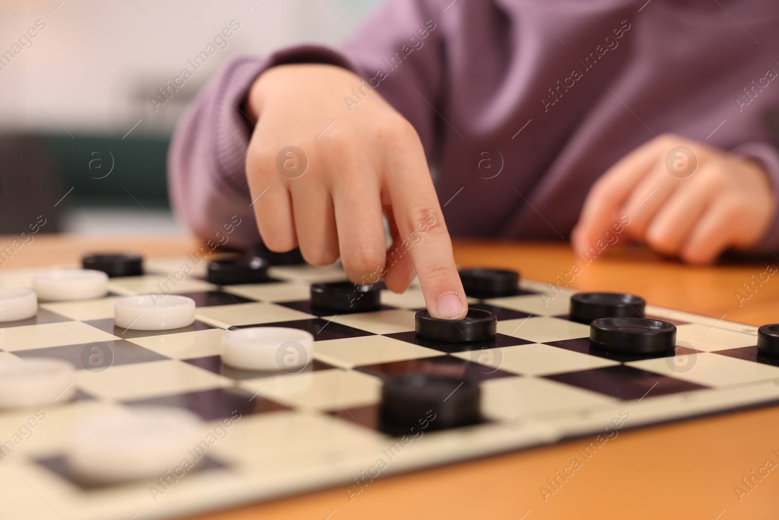 Photo of Boy playing checkers at wooden table indoors, closeup