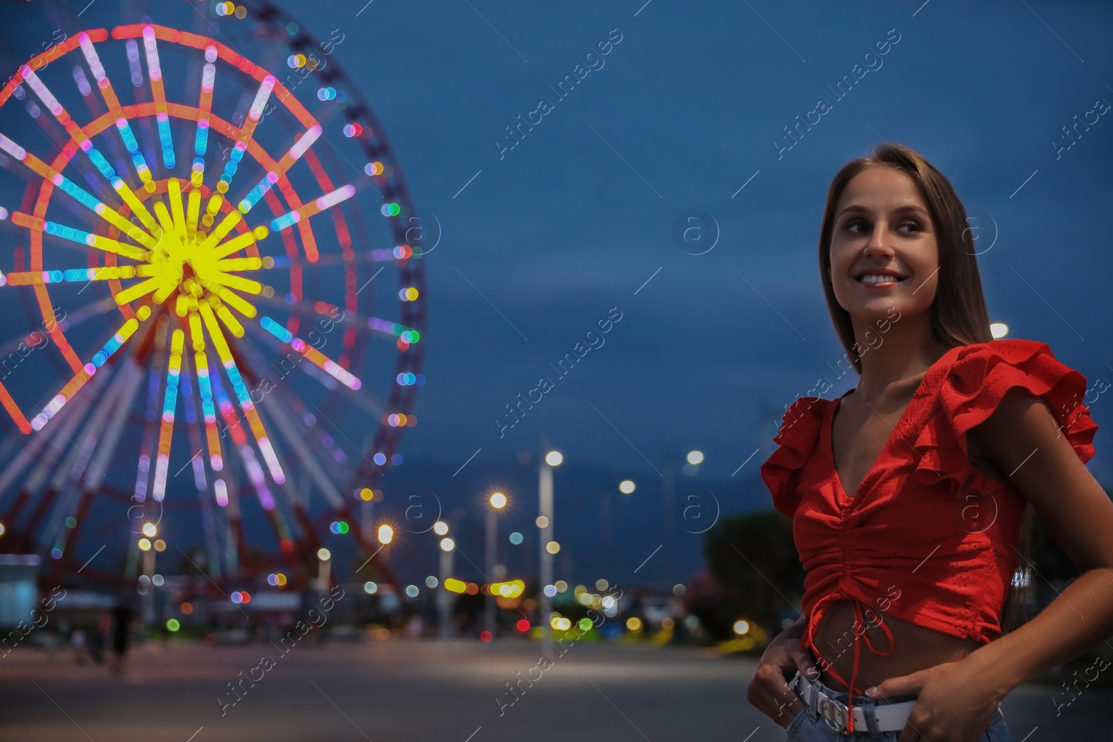 Photo of Beautiful young woman against glowing Ferris wheel in amusement park, space for text