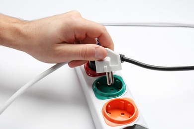 Photo of Man inserting power plug into extension cord on white background, closeup. Electrician's professional equipment