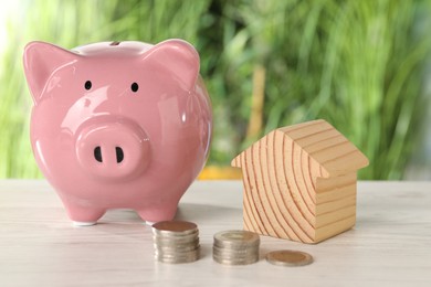 Photo of Wooden house model, stacked coins and piggy bank on light table outdoors