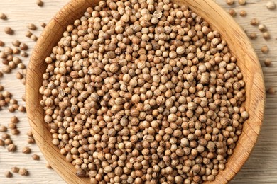 Dried coriander seeds in bowl on wooden table, top view