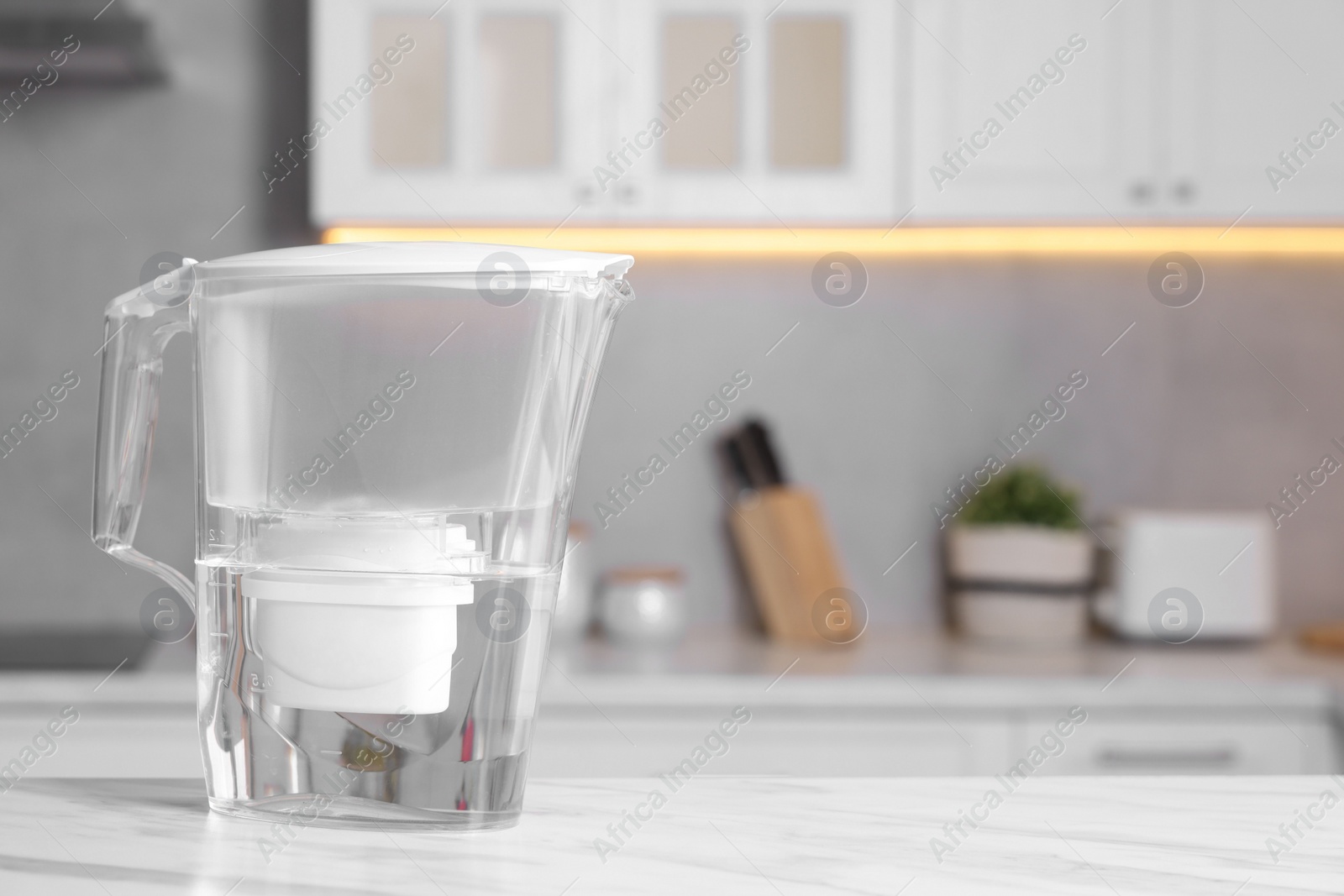 Photo of Water filter jug on white marble table in kitchen, closeup. Space for text