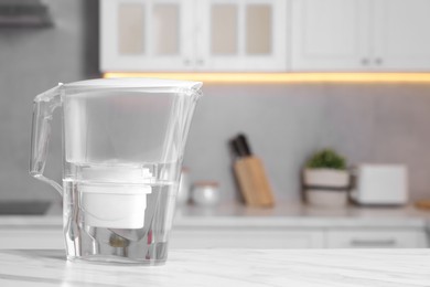 Photo of Water filter jug on white marble table in kitchen, closeup. Space for text