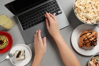Photo of Bad eating habits. Woman using laptop surrounded by different snacks at grey table, top view