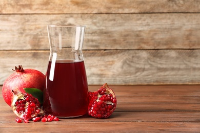 Jug of pomegranate juice and fresh fruits on table against wooden background, space for text