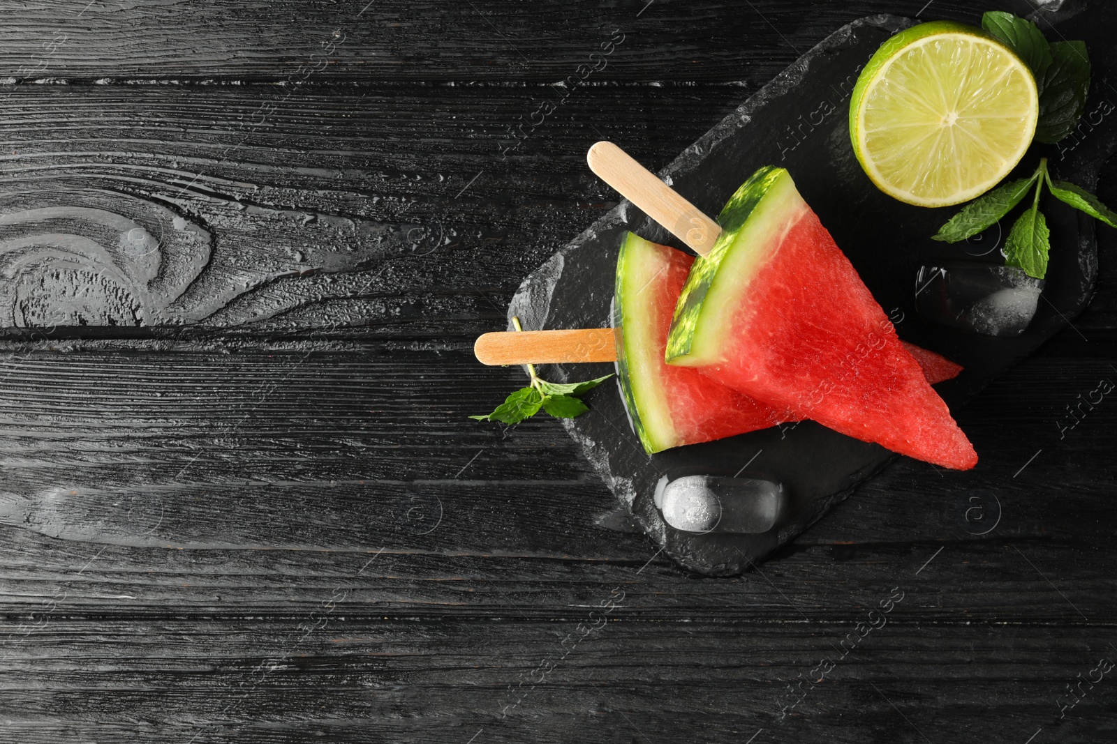 Photo of Slate board with juicy watermelon, ice and lime on black wooden table, flat lay. Space for text