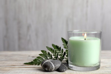 Burning candle, fern leaf and stones on white wooden table. Space for text