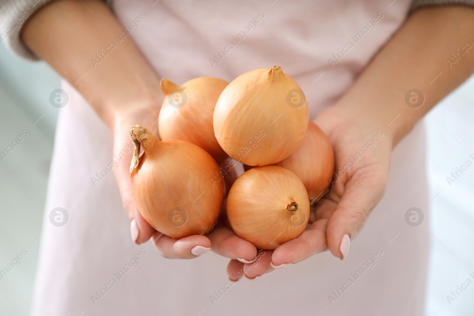 Photo of Woman holding golden onions on blurred background, closeup