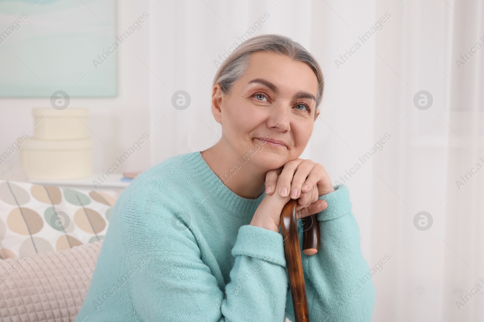 Photo of Senior woman with walking cane sitting on sofa at home