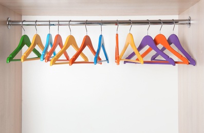 Photo of Clothes rail with colorful hangers in wardrobe