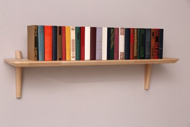 Photo of Wooden shelf with different books on light wall