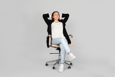 Young woman relaxing in comfortable office chair on grey background