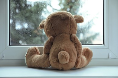 Photo of Cute lonely teddy bear on windowsill indoors, back view