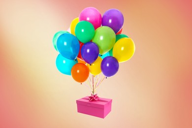 Many balloons tied to pink gift box on coral background